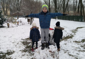 Chłopiec z rozłożonymi na boki ramionami stoi na wielkiej kuli śniegu